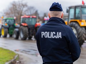 Zdjęcie przedstawia umundurowanych funkcjonariuszy z Komendy Powiatowej Policji w Leżajsku oraz pojazdy służbowe oznakowane, biorące udział w zabezpieczeniu protestu rolników w dniu dwudziestego lutego. W tle widać pojazdy oraz maszyny rolnicze.