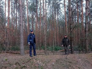 Na zdjęciu widoczni są umundurowani funkcjonariusze Policji i Straży Leśnej. Zdjęcie wykonane na zewnątrz w masywie leśnym.