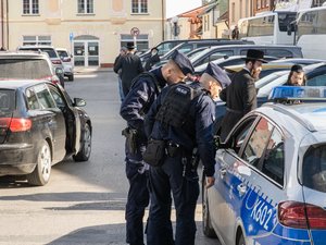 Zdjęcie przedstawia dwóch policjantów przy radiowozie podczas zabezpieczenia pielgrzymki Chasydów w Leżajsku.