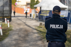 Zdjęcie przedstawia policjanta stojącego tyłem. Na plecach ma napis Policja. Zdjęcie z zabezpieczenia przyjazdu pielgrzymów chasydzkich do Leżajska.