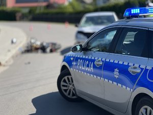 Zdjęcia przedstawiają miejsce zdarzenia drogowego, gdzie doszło do zderzenia samochodu osobowego i motoroweru. Na zdjęciach widoczny jest wóz strażacki oraz radiowóz policji.