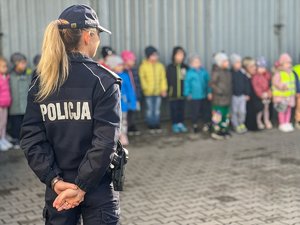 Zdjęcie przedstawia funkcjonariuszkę Komendy Powiatowej Policji w Leżajsku stojącą tyłem do fotografa. W tle widać grupę dzieci. Tło jest zamazane.