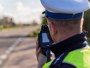 Zdjęcie przedstawia umundurowanego funkcjonariusza ruchu drogowego. który używa urządzenia kontrolno-pomiarowego. Tło jest zamazane.