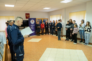 Zdjęcie przedstawia grupę osób w tym dzieci, znajdujących się a pomieszczeniu, auli. Jest to świetlica Komendy Powiatowej Policji w Leżajsku. Po lewej stronie kadru widoczni są umundurowani funkcjonariusze Policji. W centrum i po prawej stornie kadru widać osoby dorosłe i dzieci.