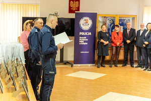 Zdjęcie przedstawia grupę osób w tym dzieci, znajdujących się a pomieszczeniu, auli. Jest to świetlica Komendy Powiatowej Policji w Leżajsku. Po lewej stronie kadru widoczni są umundurowani funkcjonariusze Policji. W centrum i po prawej stornie kadru widać osoby dorosłe i dzieci.