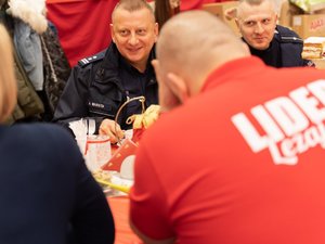 Zdjęcie przedstawia wolontariuszy Szlachetnej Paczki oraz umundurowanych funkcjonariuszy Policji. Zdjęcia przedstawiają proces pakowania paczek oraz moment przekazania ich do magazynu Szlachetnej Paczki w Leżajsku.