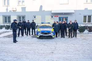 Na zdjęciu widocznych jest 14 osób , z czego 6 to umundurowani funkcjonariusze Komendy Powiatowej Policji w Leżajsku. Pozostałe osoby to ubrani na wyjściowo samorządowcy. Pomiędzy nimi znajduje się oznakowany radiowóz policyjny. Zdjęcie wykonane na zewnątrz w porze zimowej. Samochód jak i wszystkie osoby stoją frontem do kadru.