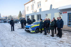 Na zdjęciu widocznych jest 14 osób , z czego 6 to umundurowani funkcjonariusze Komendy Powiatowej Policji w Leżajsku. Pozostałe osoby to ubrani na wyjściowo samorządowcy. Pomiędzy nimi znajduje się oznakowany radiowóz policyjny. Zdjęcie wykonane na zewnątrz w porze zimowej.