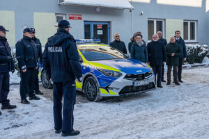 Na zdjęciu widocznych jest 12 osób , z czego 4 to umundurowani funkcjonariusze Komendy Powiatowej Policji w Leżajsku. Pozostałe osoby to ubrani na wyjściowo samorządowcy. Pomiędzy nimi znajduje się oznakowany radiowóz policyjny. Zdjęcie wykonane na zewnątrz w porze zimowej.