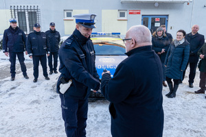 Na zdjęciu widocznych jest 8 osób, z czego 4 to umundurowani funkcjonariusze Komendy Powiatowej Policji w Leżajsku. Pozostałe osoby to ubrani na wyjściowo samorządowcy. Pomiędzy nimi znajduje się oznakowany radiowóz policyjny. Zdjęcie wykonane na zewnątrz w porze zimowej.