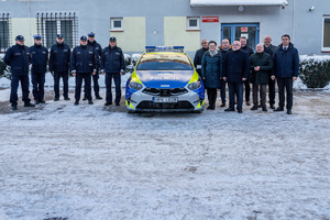 Na zdjęciu widocznych jest 14 osób , z czego 6 to umundurowani funkcjonariusze Komendy Powiatowej Policji w Leżajsku. Pozostałe osoby to ubrani na wyjściowo samorządowcy. Pomiędzy nimi znajduje się oznakowany radiowóz policyjny. Zdjęcie wykonane na zewnątrz w porze zimowej. Samochód jak i wszystkie osoby stoją frontem do kadru.