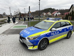 Na zdjęciu widoczny jest oznakowany radiowóz oraz uczestnicy spotkania z policjantami leżajskiej komendy. Zdjęcie zrobione na zewnątrz.