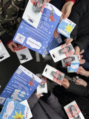 Na zdjęciu widoczni są uczestnicy spotkania z policjantami leżajskiej komendy, trzymający w ręce ulotki i oświetlenie rowerowe. Zdjęcie zrobione na zewnątrz.