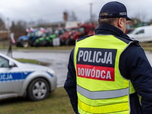 Zdjęcie przedstawia umundurowanych funkcjonariuszy z Komendy Powiatowej Policji w Leżajsku oraz pojazdy służbowe oznakowane, biorące udział w zabezpieczeniu protestu rolników w dniu dwudziestego lutego. W tle widać pojazdy oraz maszyny rolnicze.