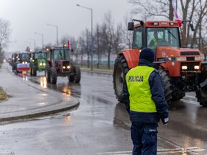 Zdjęcie przedstawia umundurowanych funkcjonariuszy z Komendy Powiatowej Policji w Leżajsku oraz pojazdy służbowe oznakowane, biorące udział w zabezpieczeniu protestu rolników w dniu dwudziestego lutego. W tle widać pojazdy oraz maszyny rolnicze.