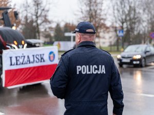 Zdjęcie przedstawia umundurowanych funkcjonariuszy z Komendy Powiatowej Policji w Leżajsku oraz pojazdy służbowe oznakowane, biorące udział w zabezpieczeniu protestu rolników w dniu dwudziestego lutego. W tle widać pojazdy oraz maszyny rolnicze.