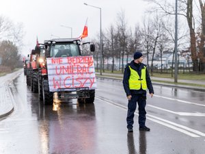 Zdjęcie przedstawia umundurowanych funkcjonariuszy z Komendy Powiatowej Policji w Leżajsku oraz pojazdy służbowe oznakowane, biorące udział w zabezpieczeniu protestu rolników w dniu dwudziestego lutego. W tle widać pojazdy oraz maszyny rolnicze.