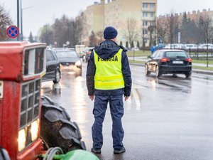 Zdjęcie przedstawia umundurowanych funkcjonariuszy z Komendy Powiatowej Policji w Leżajsku oraz pojazdy służbowe oznakowane, biorące udział w zabezpieczeniu protestu rolników w dniu dwudziestego lutego. W tle widać pojazdy oraz maszyny rolnicze.