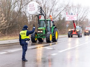 Zdjęcie przedstawia umundurowanych funkcjonariuszy z Komendy Powiatowej Policji w Leżajsku oraz pojazdy służbowe oznakowane, biorące udział w zabezpieczeniu protestu rolników w dniu dwudziestego lutego. W tle widać pojazdy oraz maszyny rolnicze.