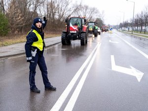 Zdjęcie przedstawia umundurowanych funkcjonariuszy z Komendy Powiatowej Policji w Leżajsku oraz pojazdy służbowe oznakowane, biorące udział w zabezpieczeniu protestu rolników w dniu dwudziestego lutego. W tle widać pojazdy oraz maszyny rolnicze.