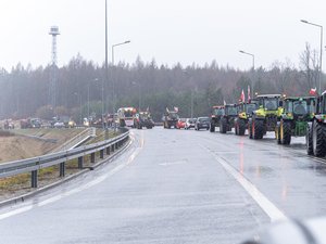 Zdjęcie przedstawia umundurowanych funkcjonariuszy z Komendy Powiatowej Policji w Leżajsku oraz pojazdy służbowe oznakowane, biorące udział w zabezpieczeniu protestu rolników w dniu dwudziestego lutego. W tle widać pojazdy oraz maszyny rolnicze.