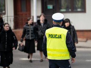 Zdjęcia przedstawiają umundurowanych policjantów z leżajskiej komendy. Są oni odwróceni tyłem do obiektywu aparatu. W tle widać pielgrzymujących do leżajska chasydów. Są oni zamazani. Widoczne też są samochody, również zamazane.