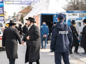 Zdjęcia przedstawiają umundurowanych policjantów z leżajskiej komendy. Są oni odwróceni tyłem do obiektywu aparatu. W tle widać pielgrzymujących do leżajska chasydów. Są oni zamazani. Widoczne też są samochody, również zamazane.