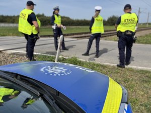 Na zdjęciu widoczni są umundurowani funkcjonariusze Policji i Straży Ochrony Kolei. Zdjęcie wykonane na zewnątrz.