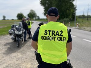 Na zdjęciu widoczni są umundurowani funkcjonariusze Policji i Straży Ochrony Kolei. Zdjęcie wykonane na zewnątrz.