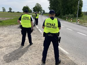 Na zdjęciu widoczni są umundurowani funkcjonariusze Policji i Straży Ochrony Kolei. Zdjęcie wykonane na zewnątrz.