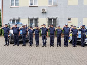 Zdjęcia przedstawiają umundurowanych funkcjonariuszy Komendy Powiatowej Policji w Leżajsku. Policjanci stoją na zewnątrz i oddają honory, przykładając  2 palce prawej dłoni do czapka z daszkiem, na którym znajduje się wyhaftowany Polski Orzełek. W tle widoczne są radiowozu oznakowane i budynek komendy.