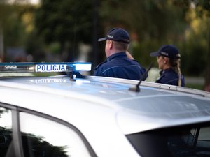 Zdjęcia przedstawiają umundurowanych funkcjonariuszy policji stojących w postawie zasadniczej. W tle widać włączone sygnały błyskowe.