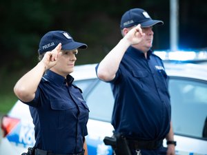 Zdjęcia przedstawiają umundurowanych funkcjonariuszy policji stojących w postawie zasadniczej. W tle widać włączone sygnały błyskowe.