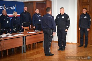 Zdjęcia przedstawiają umundurowanych funkcjonariuszy Policji w trakcie przebiegu eliminacji do ogólnopolskiego konkursu służby dyżurnej. Na zdjęciach widać zmagania policjantów podczas testów i zadań praktycznych. Wszystko odbywa się w zamkniętej sali konferencyjnej.