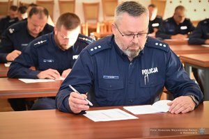 Zdjęcia przedstawiają umundurowanych funkcjonariuszy Policji w trakcie przebiegu eliminacji do ogólnopolskiego konkursu służby dyżurnej. Na zdjęciach widać zmagania policjantów podczas testów i zadań praktycznych. Wszystko odbywa się w zamkniętej sali konferencyjnej.