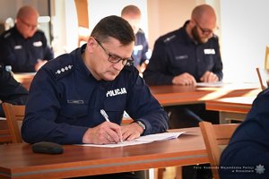 Zdjęcia przedstawiają umundurowanych funkcjonariuszy Policji w trakcie przebiegu eliminacji do ogólnopolskiego konkursu służby dyżurnej. Na zdjęciach widać zmagania policjantów podczas testów i zadań praktycznych. Wszystko odbywa się w zamkniętej sali konferencyjnej.