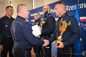 Zdjęcia przedstawiają umundurowanych funkcjonariuszy Policji w trakcie przebiegu eliminacji do ogólnopolskiego konkursu służby dyżurnej. Na zdjęciach widać zmagania policjantów podczas testów i zadań praktycznych. Wszystko odbywa się w zamkniętej sali konferencyjnej.