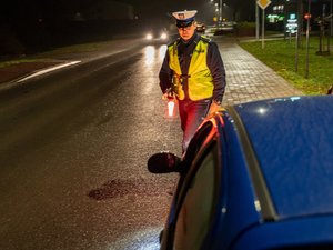 Zdjęcia przedstawiają umundurowanych funkcjonariuszy podczas akcji &amp;quot;Twoje światła-nasze bezpieczeństwo&amp;quot;. Zdjęcie robione nocą. Policjant jest ubrany w odblaskową kamizelkę i kontroluje pojazd.