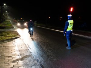 Zdjęcia przedstawiają umundurowanych funkcjonariuszy podczas akcji &amp;quot;Twoje światła-nasze bezpieczeństwo&amp;quot;. Zdjęcie robione nocą. Policjant jest ubrany w odblaskową kamizelkę i kontroluje pojazd.