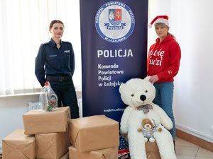 Zdjęcia przedstawiają funkcjonariuszki z Komendy Powiatowej Policji w Leżajsku podczas realizowania projektu &quot;Szlachetnej Paczki&quot;. Na zdjęciach znajdują się dwie kobiety. Jedna z nich jest ubrana w policyjny mundur, a druga w czerwoną bluzę z napisem &quot;Lubię Ludzi&quot;. Zdjęcie jest zrobione w pomieszczeniu. Widoczny jest rollup komendy.