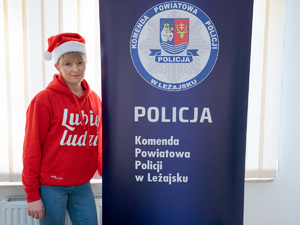 Zdjęcia przedstawiają funkcjonariuszki z Komendy Powiatowej Policji w Leżajsku podczas realizowania projektu &quot;Szlachetnej Paczki&quot;. Na zdjęciach znajdują się dwie kobiety. Jedna z nich jest ubrana w policyjny mundur, a druga w czerwoną bluzę z napisem &quot;Lubię Ludzi&quot;. Zdjęcie jest zrobione w pomieszczeniu. Widoczny jest rollup komendy.