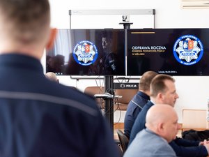 Zdjęcia przedstawia funkcjonariuszy policji wraz z samorządowcami, prokuratorem, sędzią oraz strażakiem podczas odprawy rocznej w leżajskiej komendzie. Odprawa odbyła się w budynku Komendy Powiatowej Policji w Leżajsku. Na zdjęciach znajdują się policjanci oraz osoby cywilne. Widoczny jest telewizor na którym wyświetlana jest prezentacja.