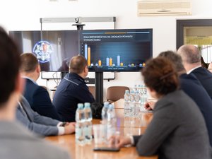 Zdjęcia przedstawia funkcjonariuszy policji wraz z samorządowcami, prokuratorem, sędzią oraz strażakiem podczas odprawy rocznej w leżajskiej komendzie. Odprawa odbyła się w budynku Komendy Powiatowej Policji w Leżajsku. Na zdjęciach znajdują się policjanci oraz osoby cywilne. Widoczny jest telewizor na którym wyświetlana jest prezentacja.