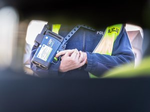 Zdjęcie przedstawia tułów policjanta Ruchu Drogowego, który w rękach trzyma urządzenie do pomiaru prędkości.