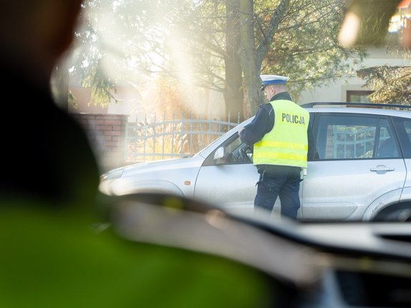 Zdjęcie przedstawia umundurowanego funkcjonariusza ruchu drogowego podczas kontroli drogowej.