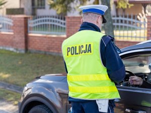 Zdjęcie przedstawia umundurowanego policjanta w trakcie kontroli drogowej