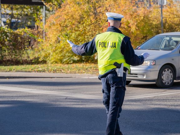 Zdjęcie przedstawia umundurowanego policjanta, podczas ręcznej regulacji ruchu w trakcie wzmożonego ruchu drogowego w dniu wszystkich świętych.