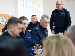 Zdjęcia przedstawiają przebieg odprawy rocznej w auli Komendy Powiatowej Policji w Leżajsku. Na zdjęciach widać umundurowanych funkcjonariuszy oraz osoby cywilne - zaproszonych gości, przedstawicieli samorządów powiatu leżajskiego. Zdjęcia wykonane są wewnątrz budynku.