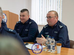 Zdjęcia przedstawiają przebieg odprawy rocznej w auli Komendy Powiatowej Policji w Leżajsku. Na zdjęciach widać umundurowanych funkcjonariuszy oraz osoby cywilne - zaproszonych gości, przedstawicieli samorządów powiatu leżajskiego. Zdjęcia wykonane są wewnątrz budynku.