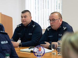 Zdjęcia przedstawiają przebieg odprawy rocznej w auli Komendy Powiatowej Policji w Leżajsku. Na zdjęciach widać umundurowanych funkcjonariuszy oraz osoby cywilne - zaproszonych gości, przedstawicieli samorządów powiatu leżajskiego. Zdjęcia wykonane są wewnątrz budynku.